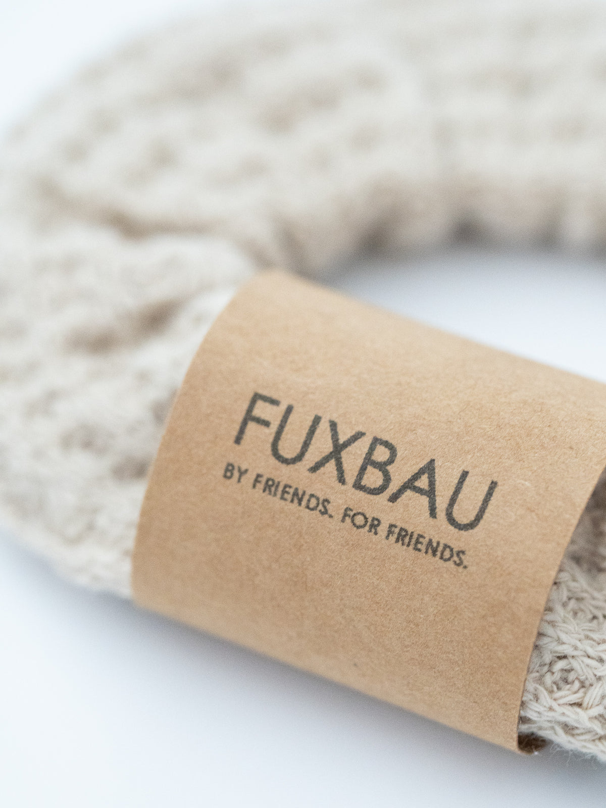 Nahaufnahme eines beigen FUXBAU Waffelstrick-Scrunchies mit Papierbanderole – fair produziert und stilvoll.