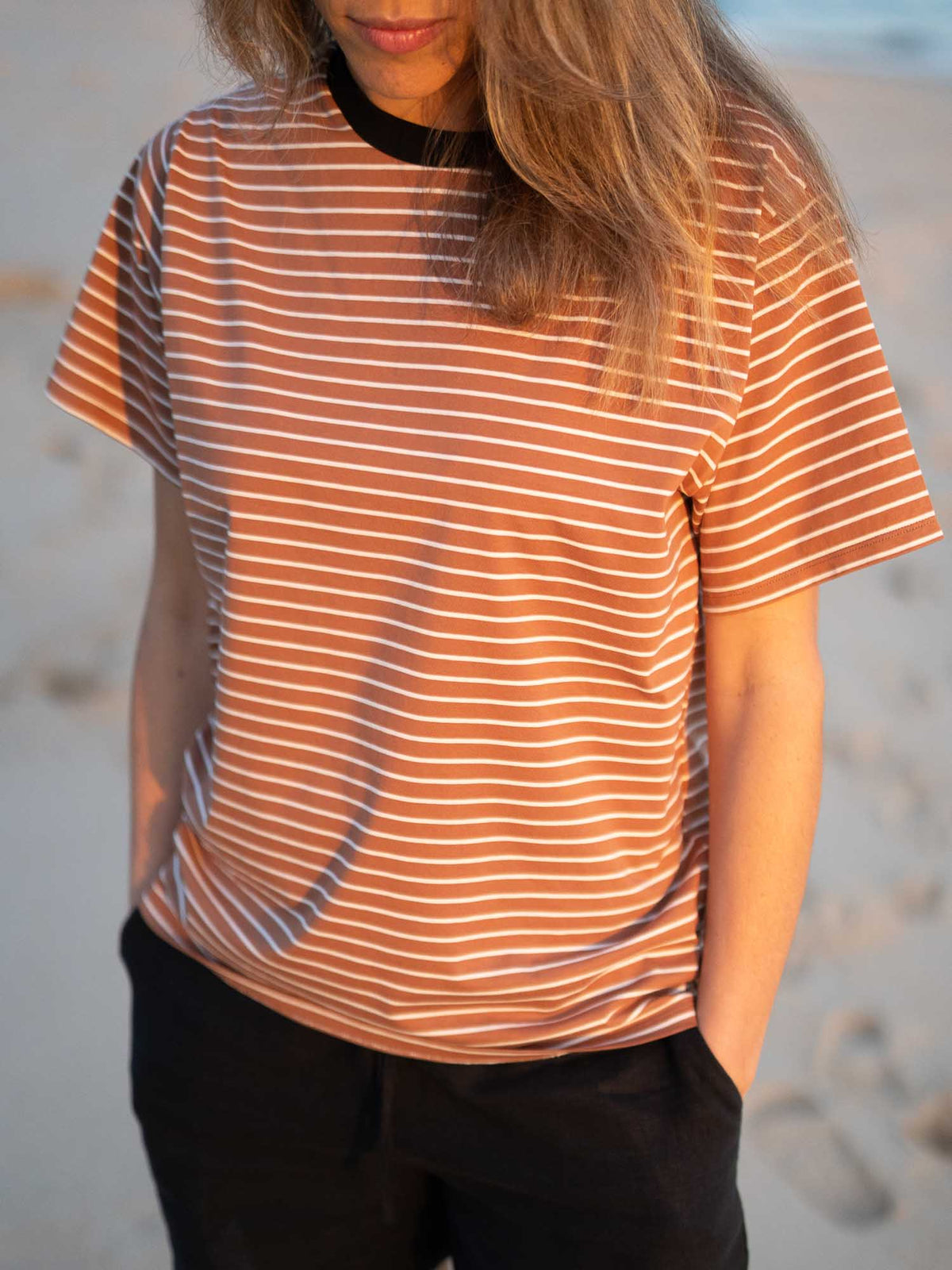 Detailansicht eines Fair Fashion Frauen T-Shirt in karamell, schwarz und weiss von FUXBAU aus Biobaumwolle. Gefertigt unter GOTS-Bedingungen in Portugal und getragen am Strand in Portugal. Getragen von einer jungen Frau am Strand in Südportugal an der Algarve.