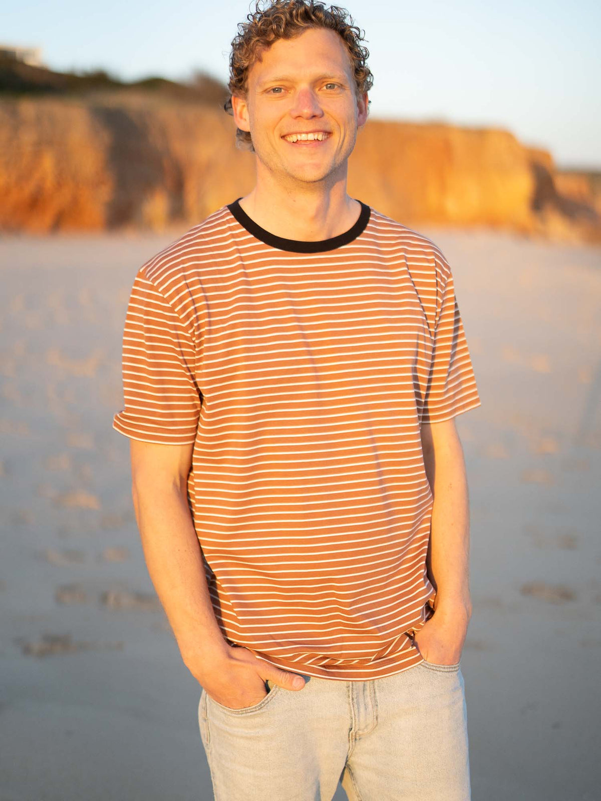 Gestreiftes Fair Fashion T-Shirt in karamell, schwarz und weiss von FUXBAU aus Biobaumwolle. Gefertigt unter GOTS-Bedingungen in Portugal und getragen am Strand in Portugal.