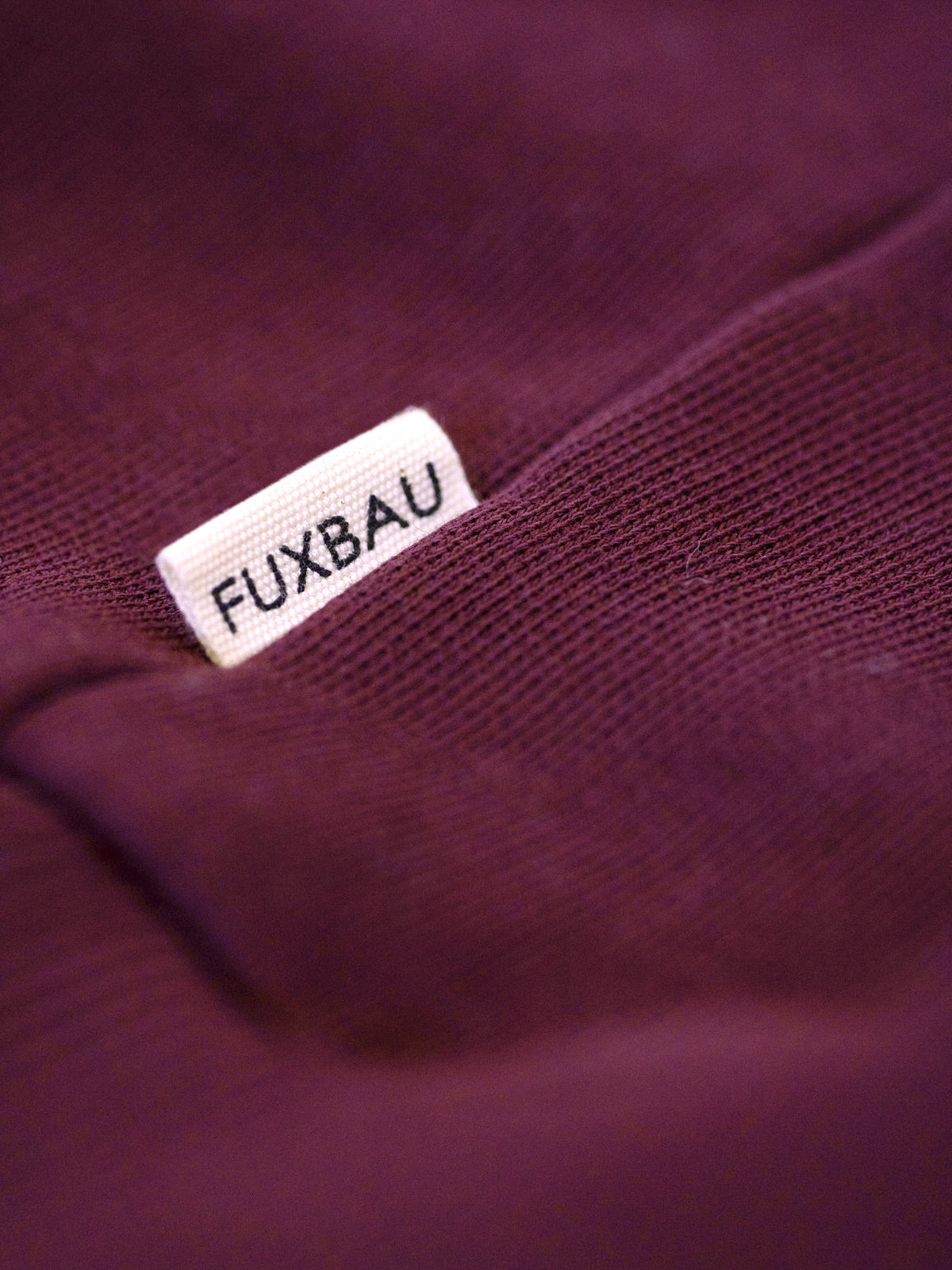 Seitliches FUXBAU Label auf Half Zip Sweater aus Bio-Baumwolle in Bordeaux – hochwertige Verarbeitung, fair gefertigt in Portugal.