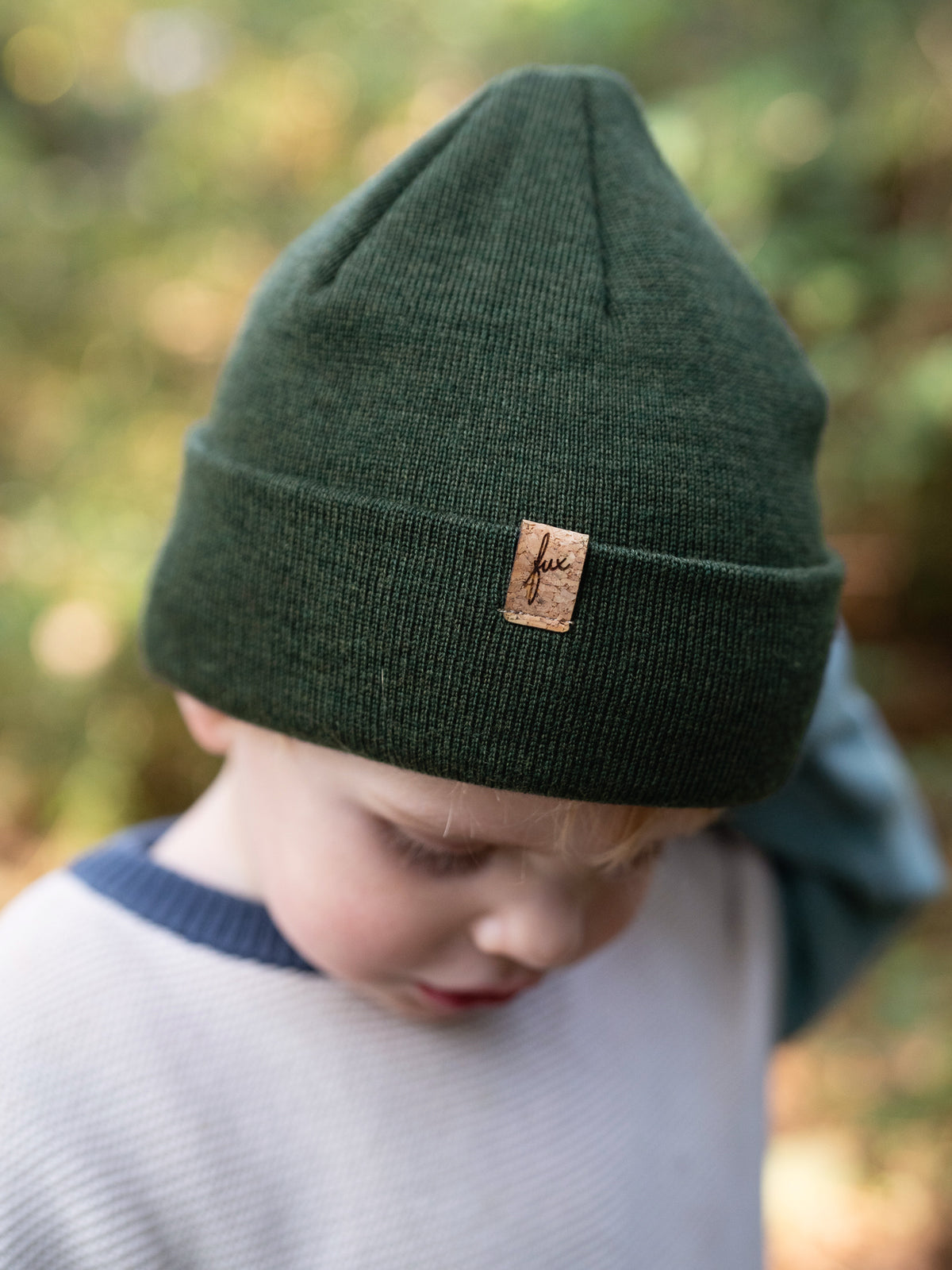 Kind trägt FUXBAU Kinder Merino Beanie in Waldgrün mit Kork-Label – fair produziert in Deutschland.