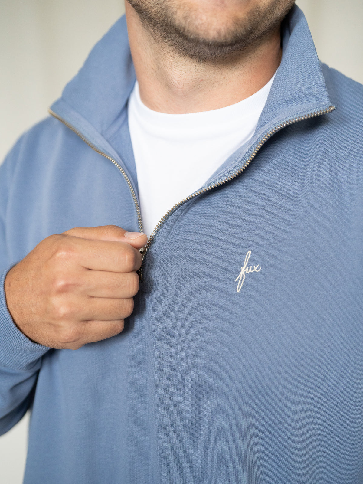 Nahaufnahme vom Zipper und gesticktem „fux“-Logo auf der Brust.