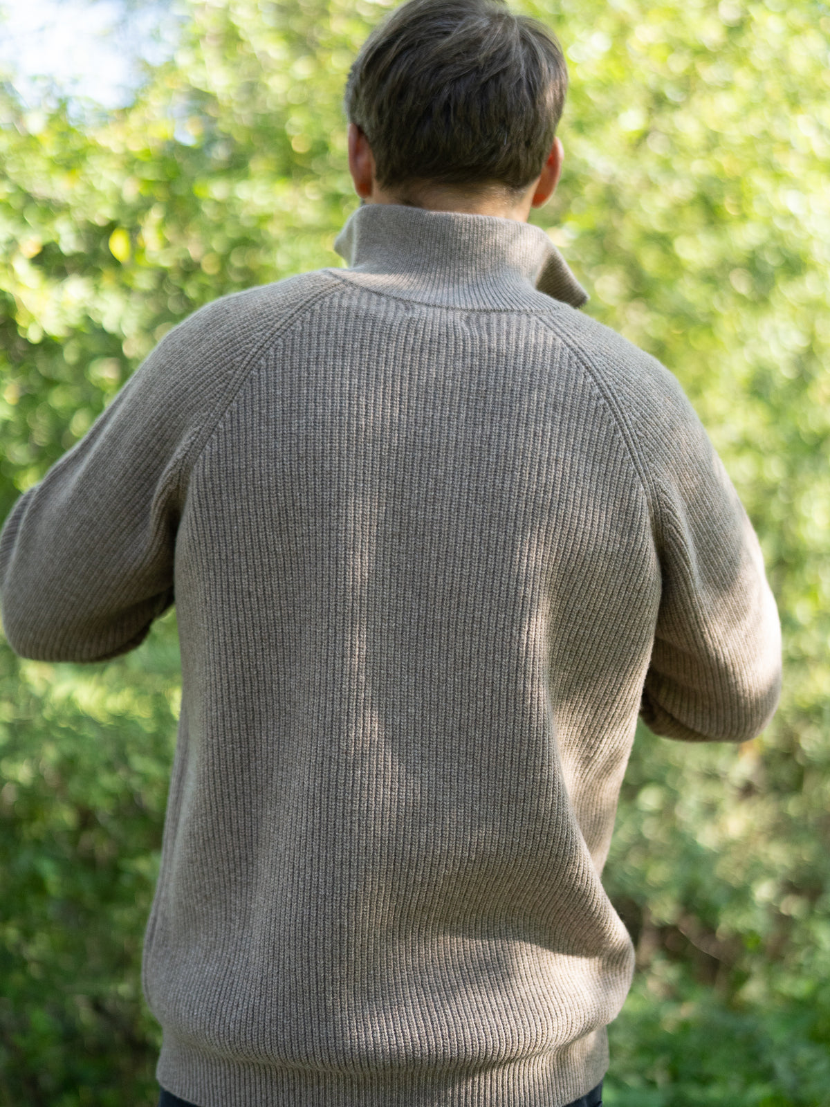 Fair Fashion Männer Merino Troyer in braun meliert aus 100% Merino Schurwolle Made in Italy, getragen von einem jungen Mann mit Rückansicht.