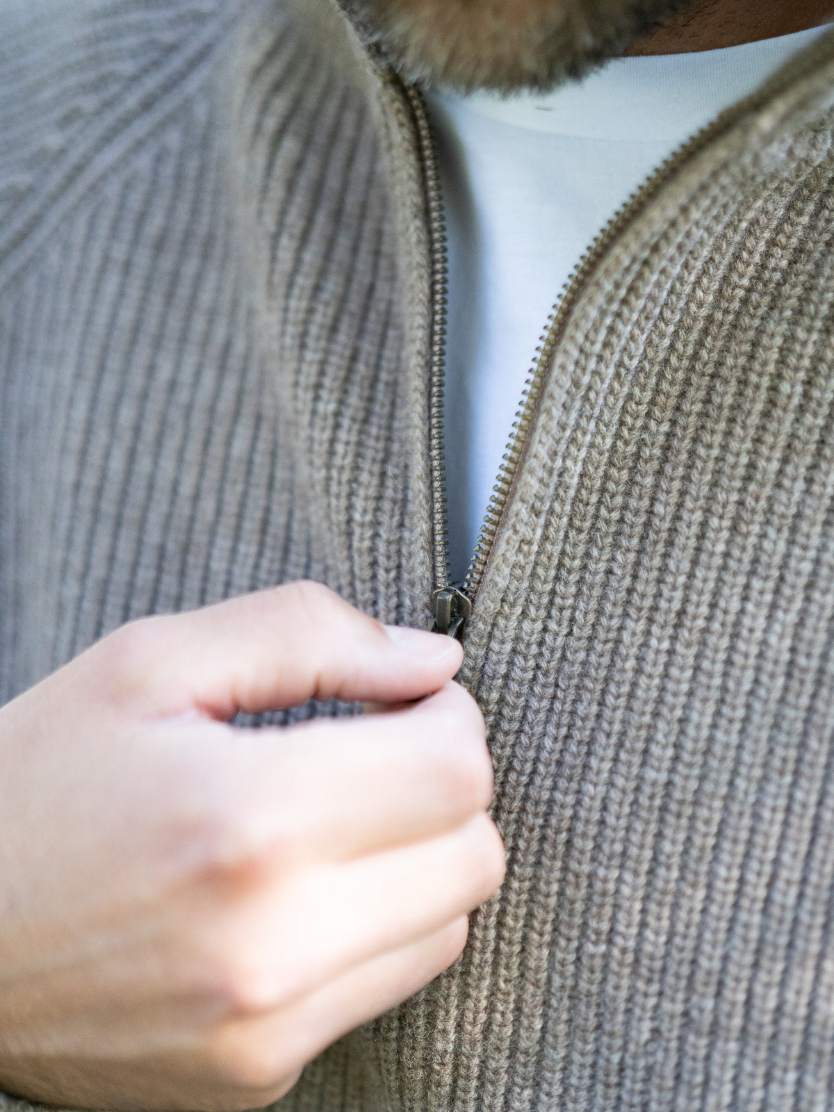 Fair Fashion Männer Merino Troyer in braun meliert aus 100% Merino Schurwolle Made in Italy, getragen von einem jungen Mann der die Hand am Reissverschluss hat.