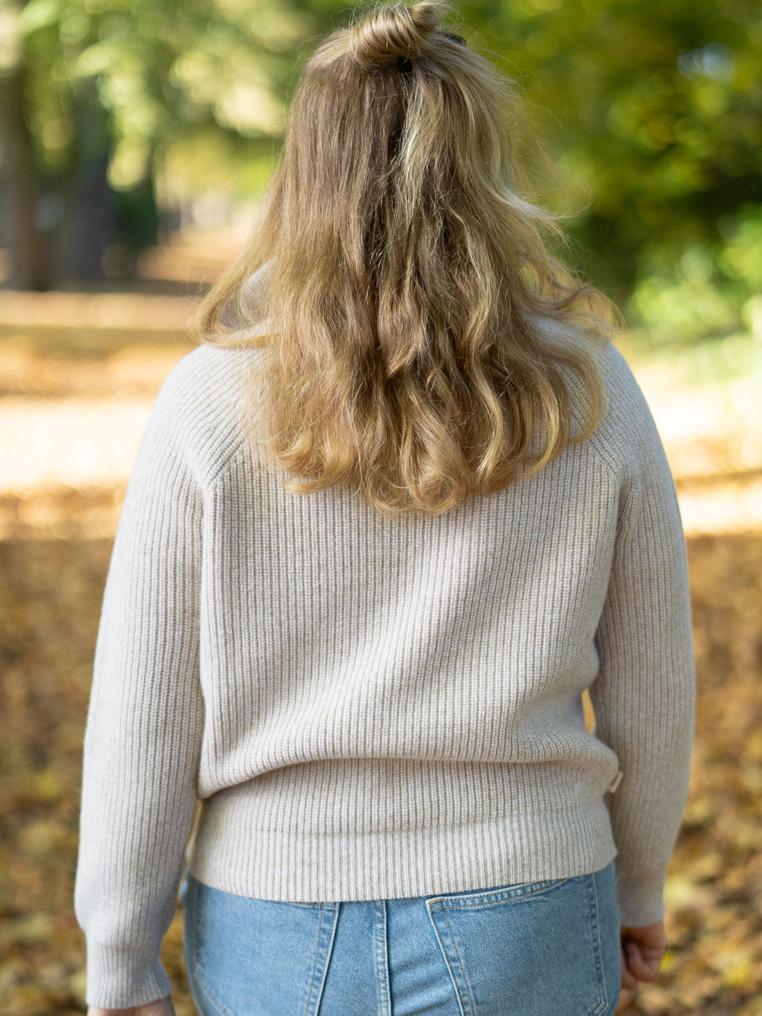 Eine junge, blonde Frau trägt einen fair produzierten Fair Fashion Troyer von FUXBAU aus 100% Merinowolle in der Natur im Herbst.