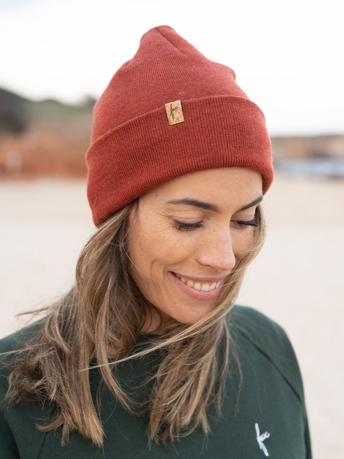 Fair Fashion Merino Kork Beanie in Herbstorange aus 100% Merino Schurwolle gestrickt in Deutschland getragen am Strand in Portugal und mit einem kleinen fux Patch aus Kork veredelt.