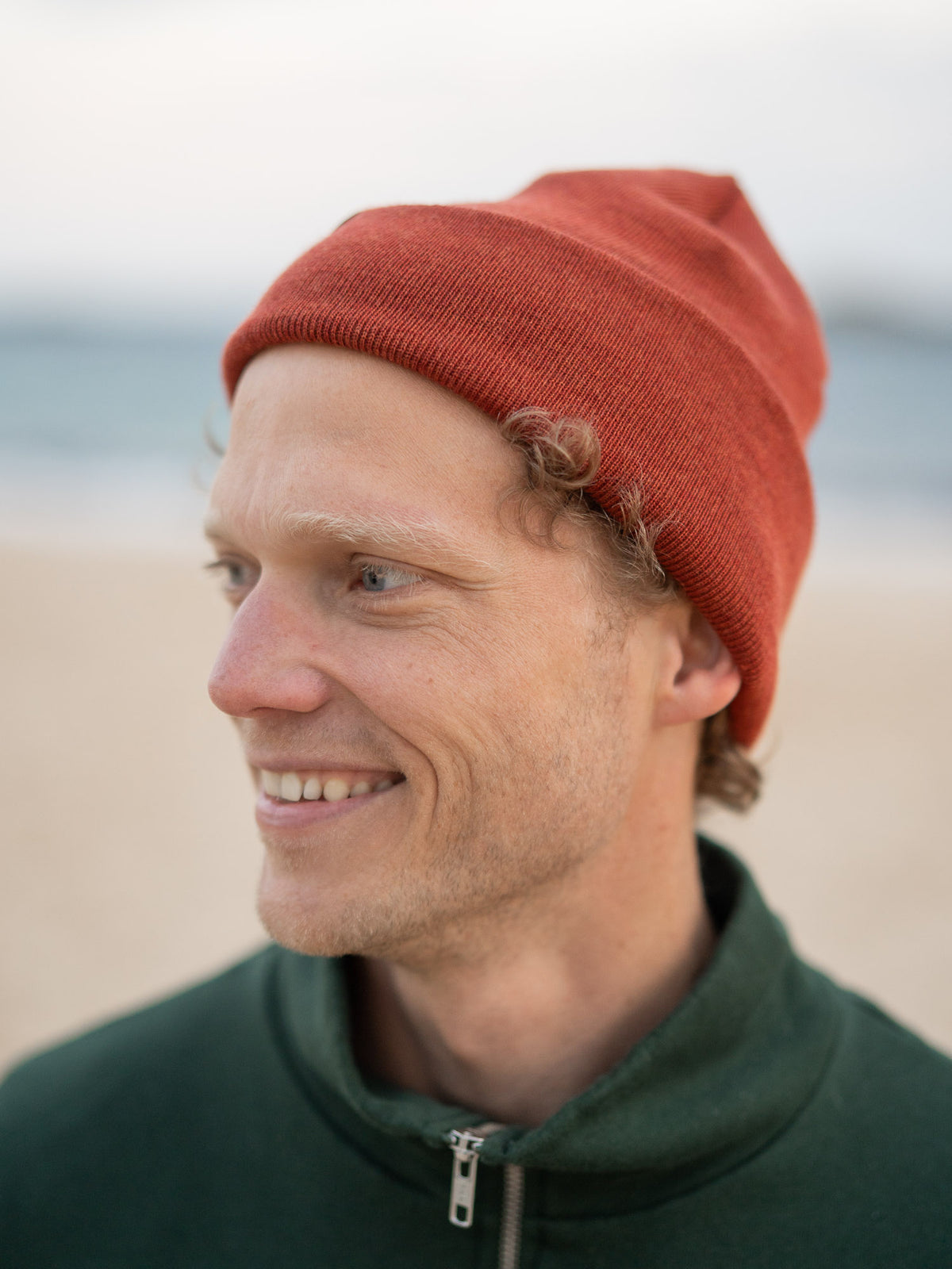 Fair Fashion Merino Kork Beanie in Herbstorange aus 100% Merino Schurwolle gestrickt in Deutschland getragen am Strand in Portugal und mit einem kleinen fux Patch aus Kork veredelt.