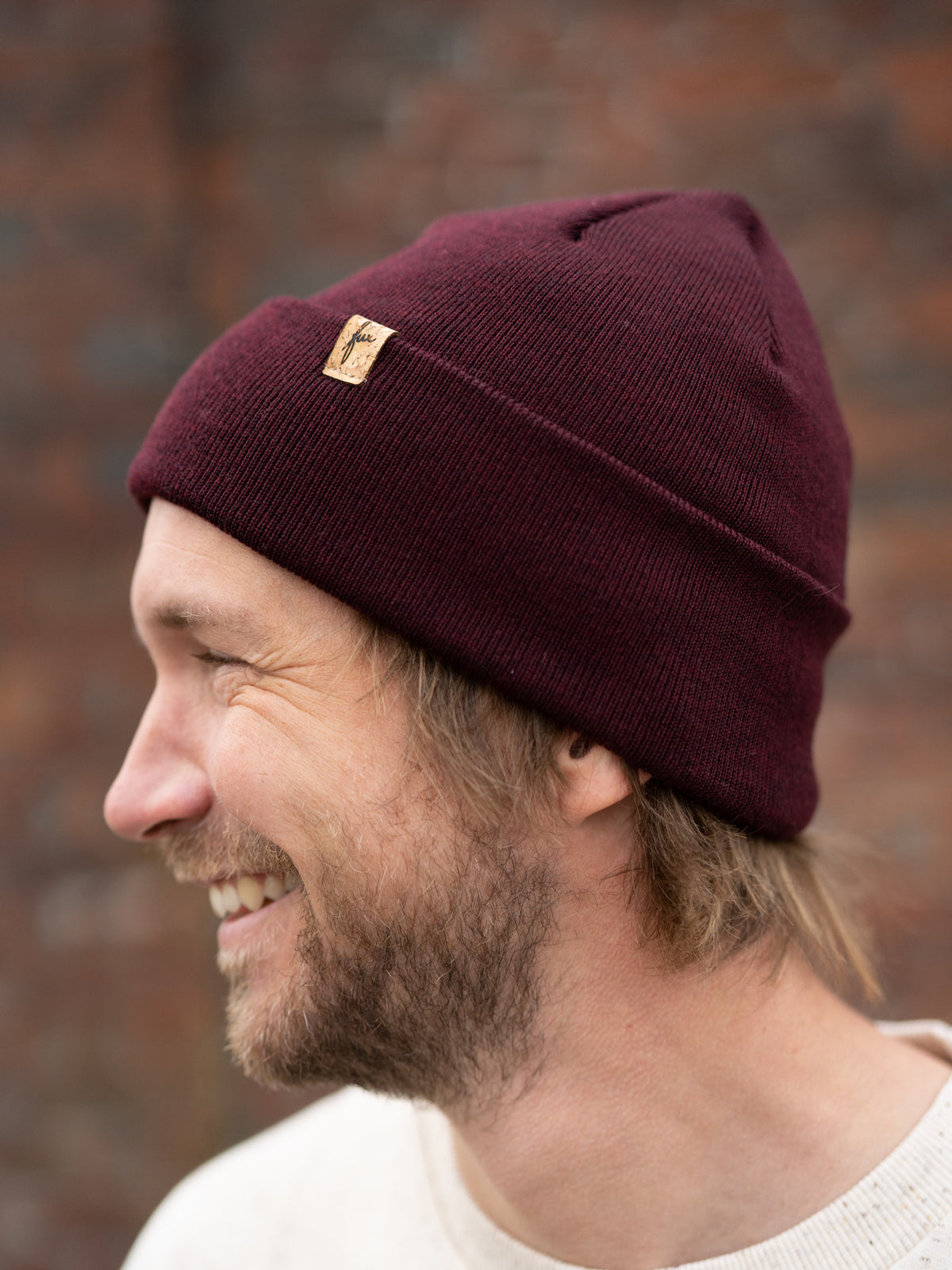 Kenny trägt eine Fair Fashion FUXBAU Merino Kork Beanie aus Merino Schurwolle gestrickt in Deutschland in Bordeaux.