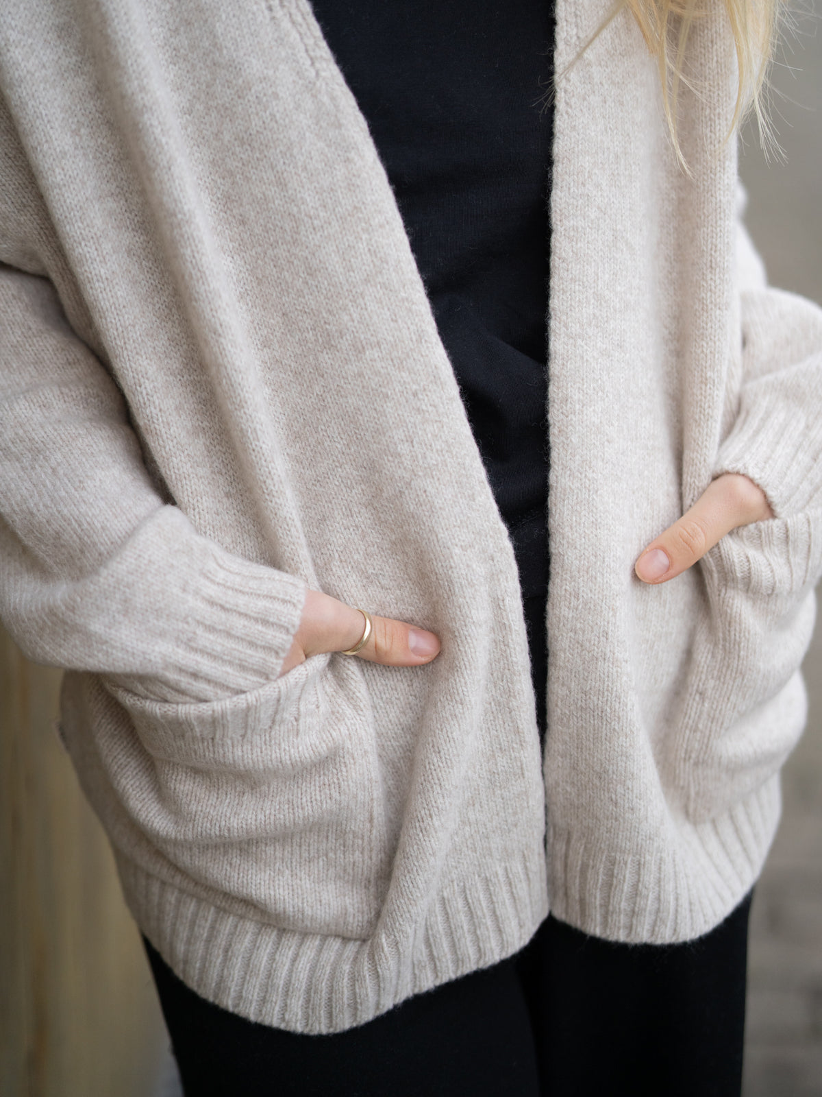 Greta hat die Hände in den gemütlichen Taschen des Frauen Oversize Merino Cardigans in beigemeliert.