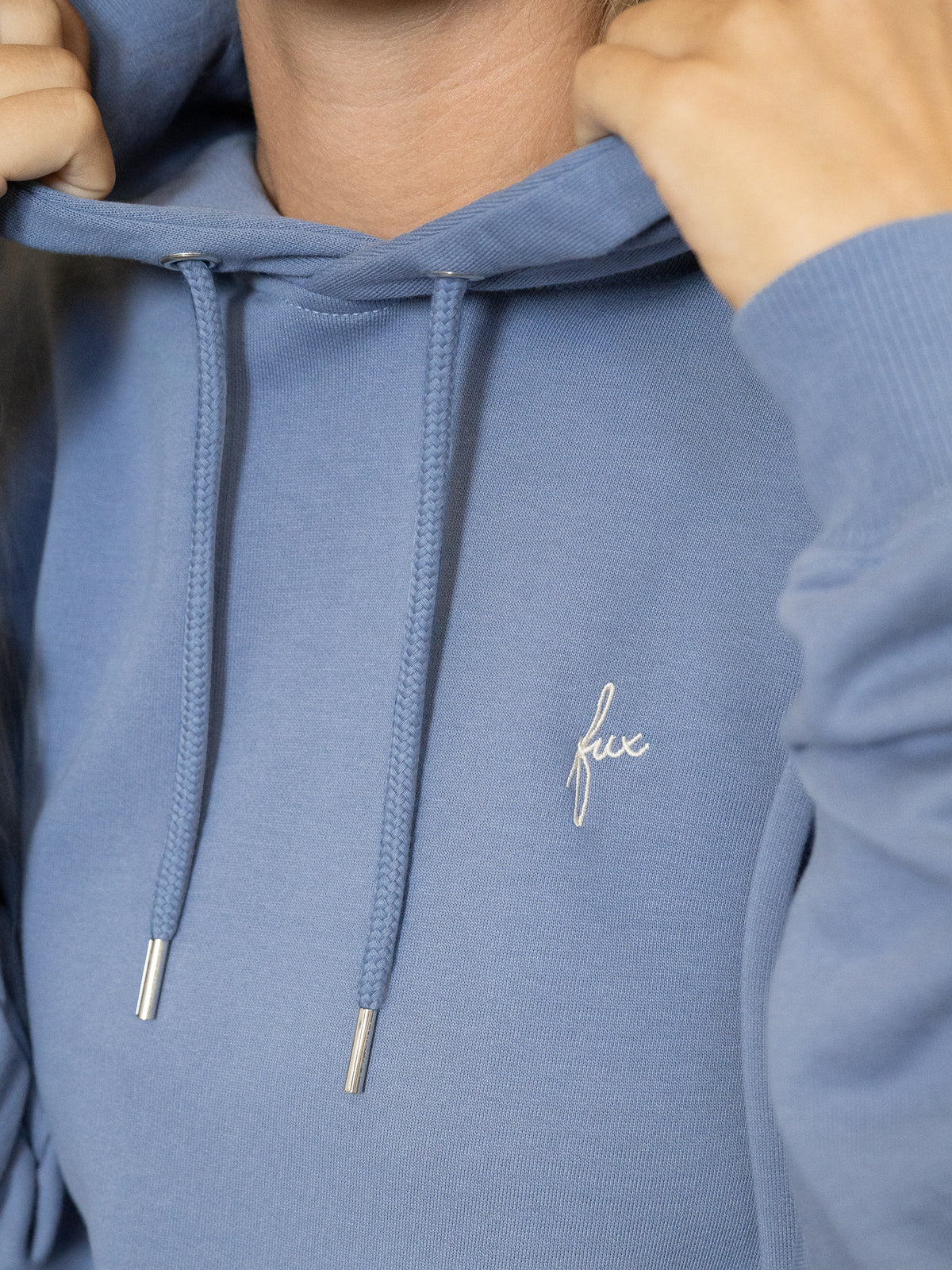 Detailansicht des Brustbereichs mit gesticktem „fux“-Logo und Kordelzug der Kapuze.
