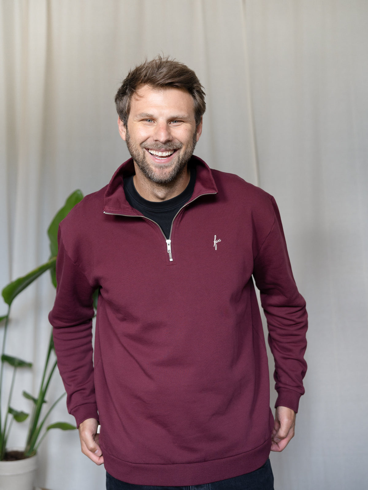 Mann trägt den bordeauxfarbenen FUXBAU Half-Zip Sweater – Fair Fashion Pullover aus Biobaumwolle, hergestellt in Portugal.