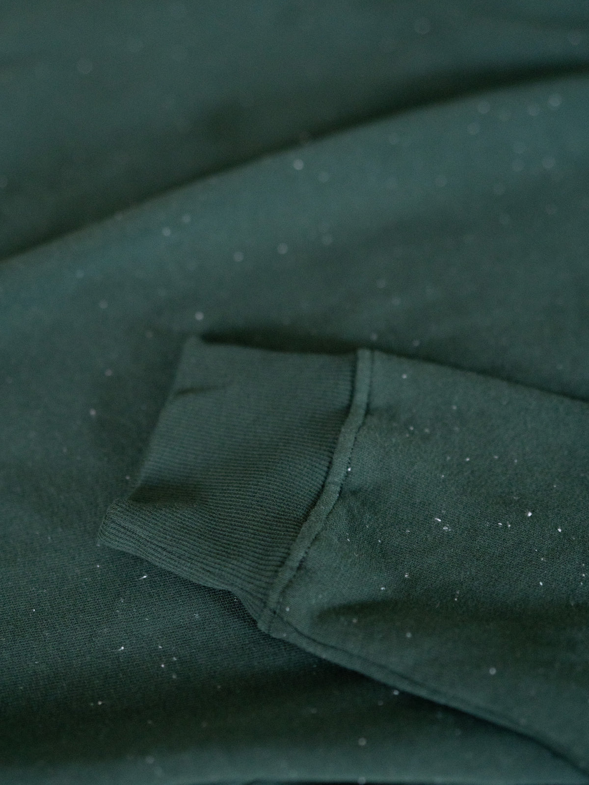 Ärmel-Detail des grünen FUXBAU Neps Pullovers aus Bio-Baumwolle – feine Struktur mit weißen Neps, gefertigt in Portugal