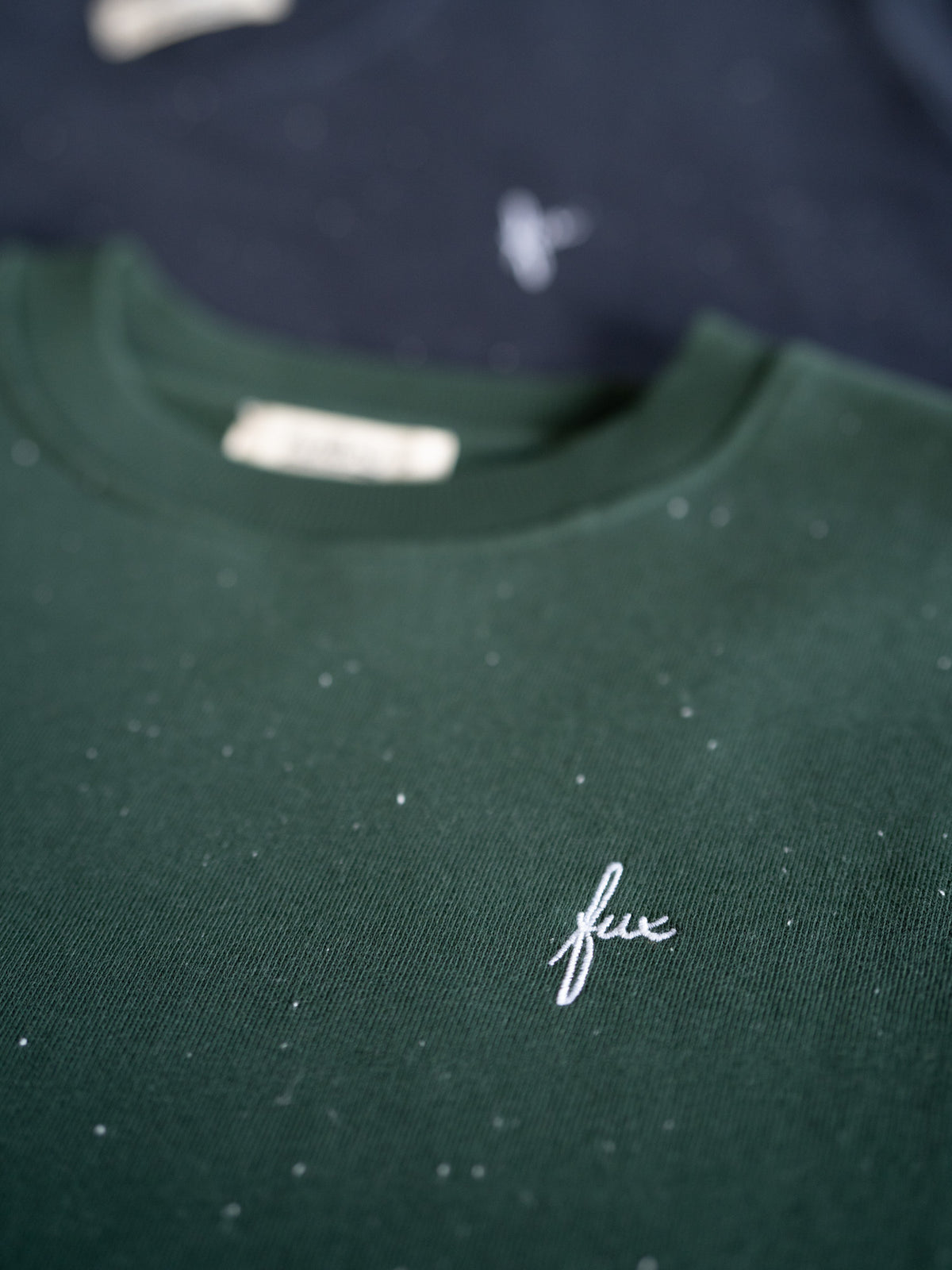 Grüner FUXBAU Neps Pullover aus Bio-Baumwolle – gesticktes FUX Logo auf der Brust, im Hintergrund Variante in Navy