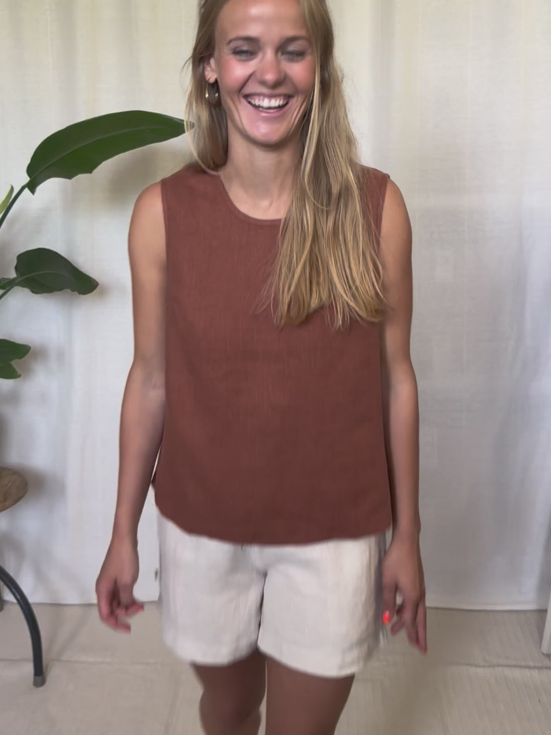Eine junge, blonde Frau trägt ein Leinentop in der farbe rotbraun von FUXBAU in Kombination mit einer cremweissen Leinenshorts. 
